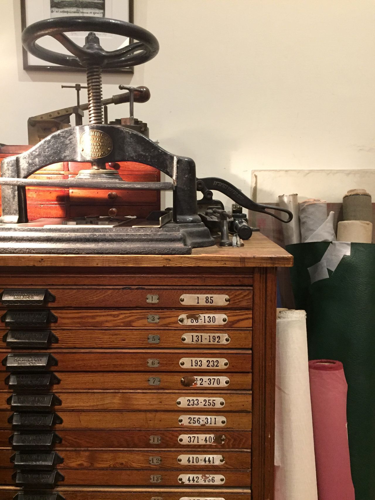 Old printing press on a wooden cabinet with labeled drawers in a workshop.