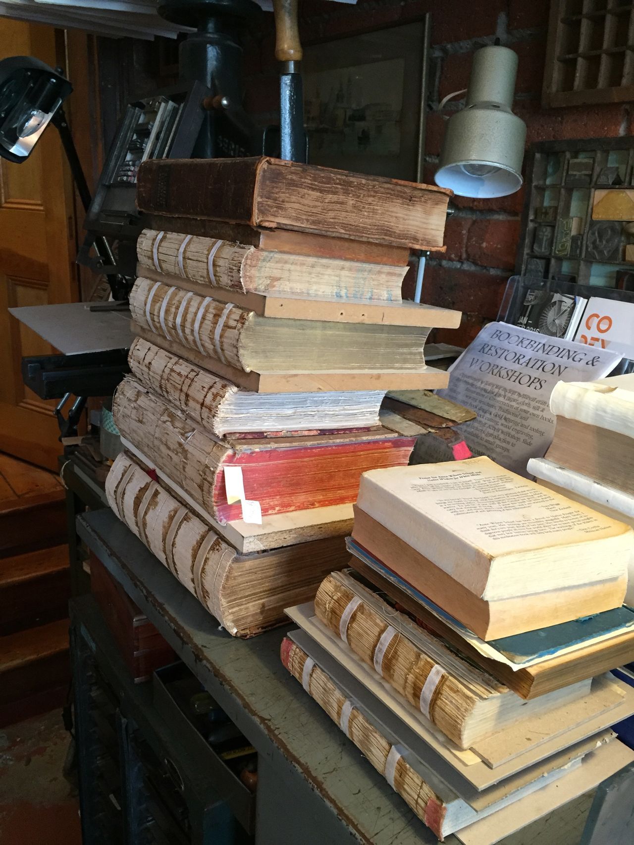 Stacks of old, worn books piled on a shelf in a dim, cluttered bookstore or library corner