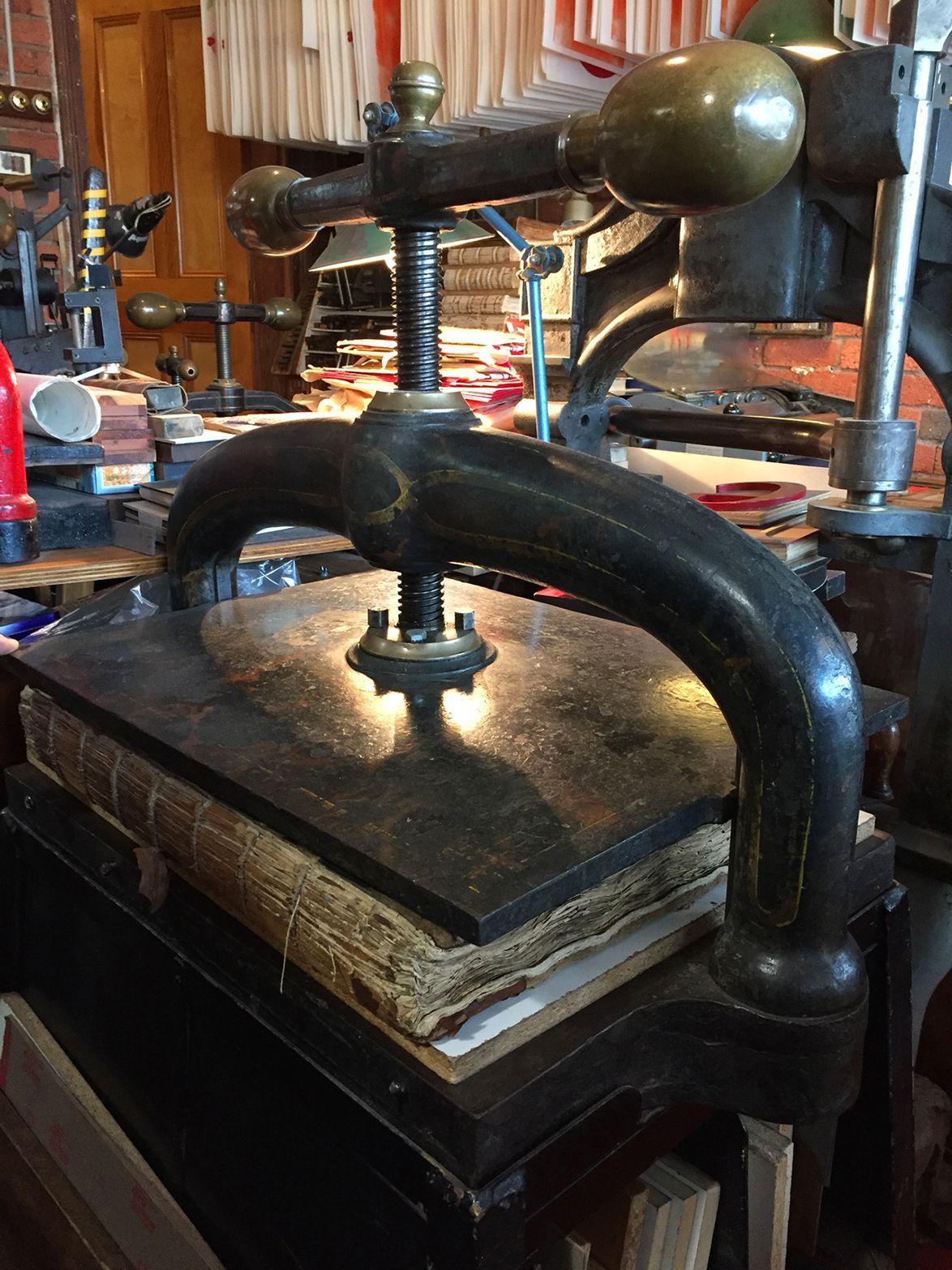 Old cast-iron press with a curved handle resting on stacked books in a cluttered workshop