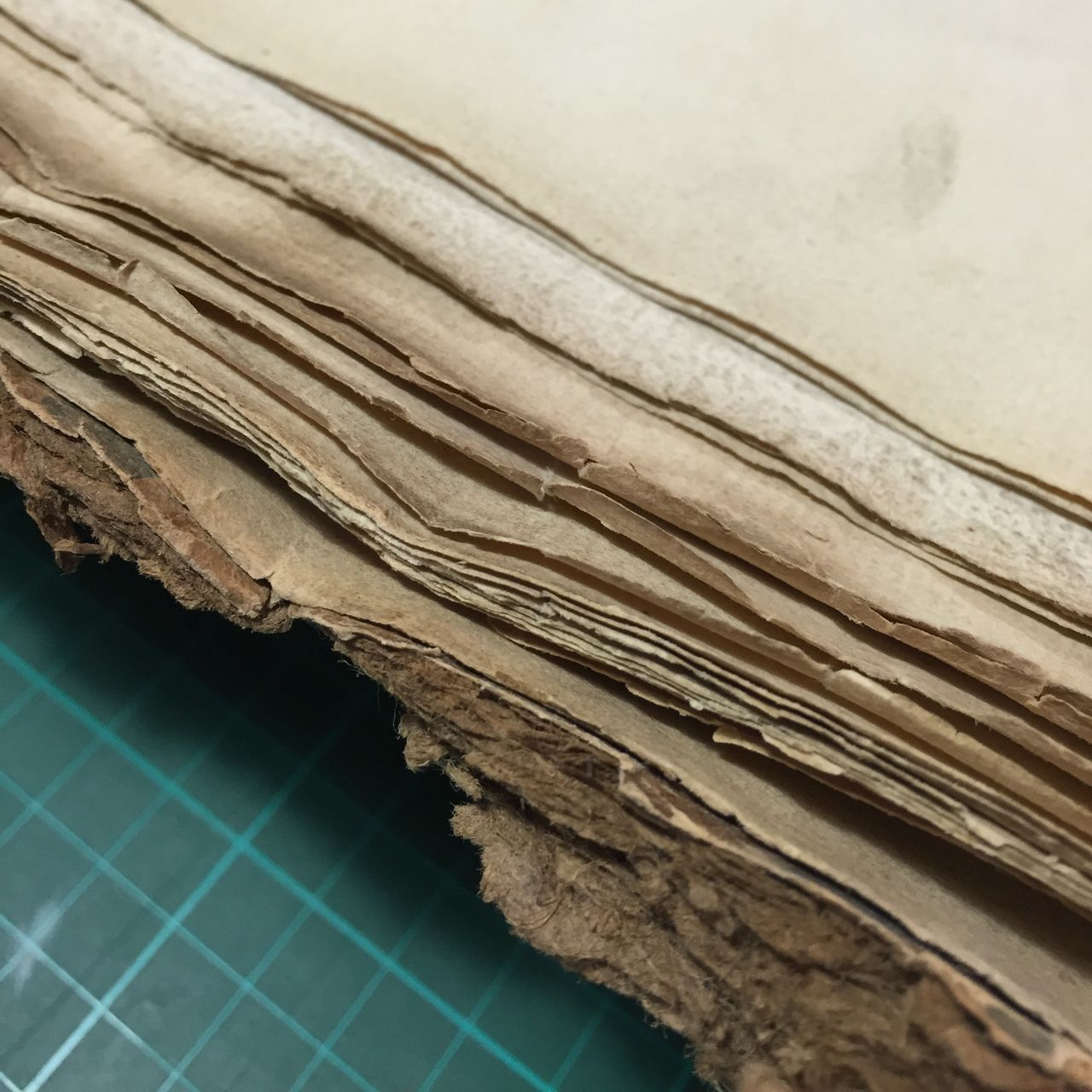 Close-up of worn, layered paper edges on a green cutting mat