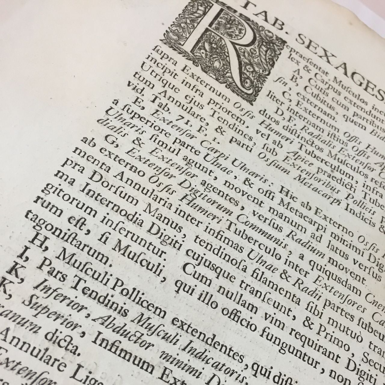 Close-up of an old Latin printed book page with ornate drop cap and dense text.