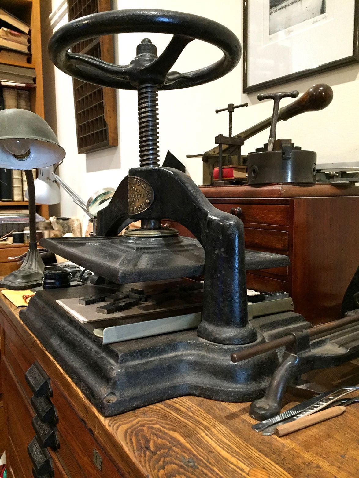 Vintage black metal press machine on a wooden desk in a workshop or office.