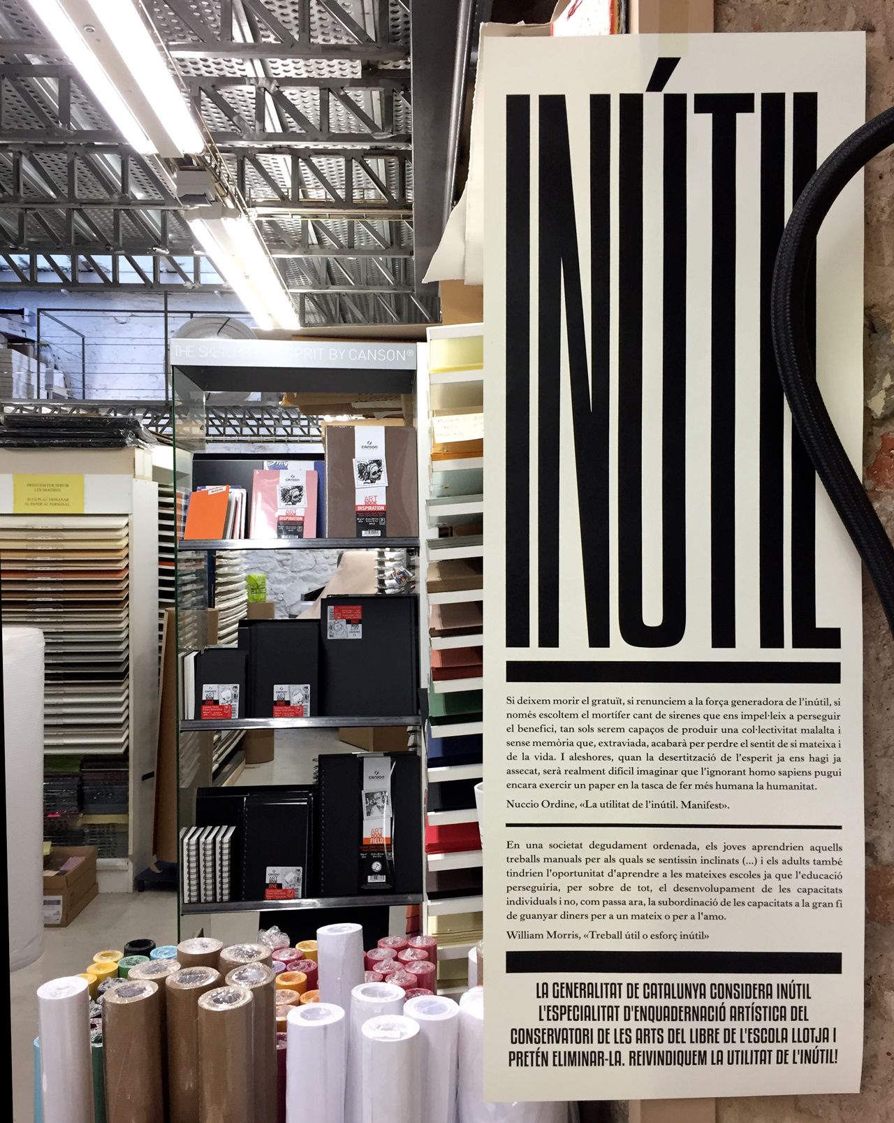 Store display with a tall beige poster featuring bold black vertical text and shelves of rolls and boxes in the background