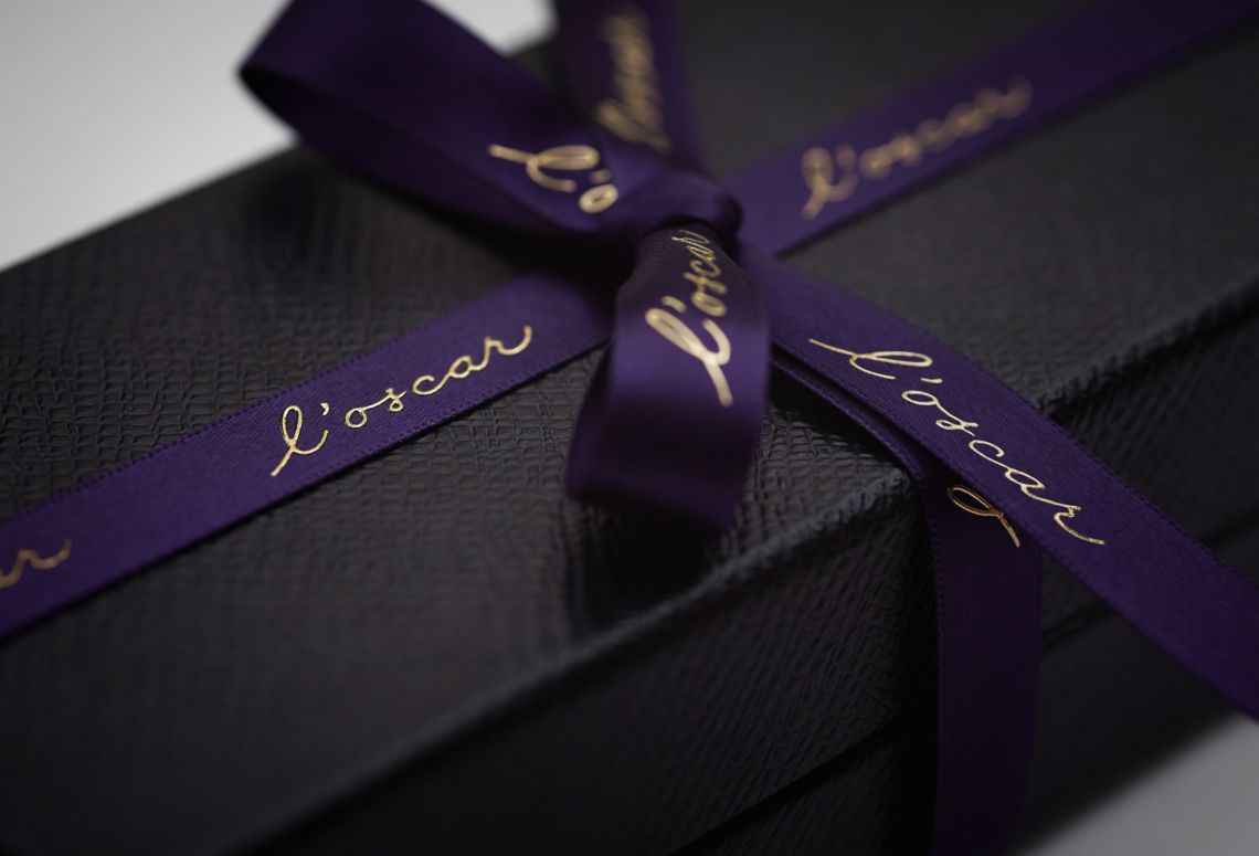 Black gift box tied with a purple ribbon and gold script lettering