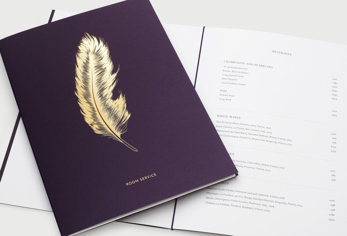 A dark purple notebook with a gold feather illustration on the cover, resting on an open page with printed text.