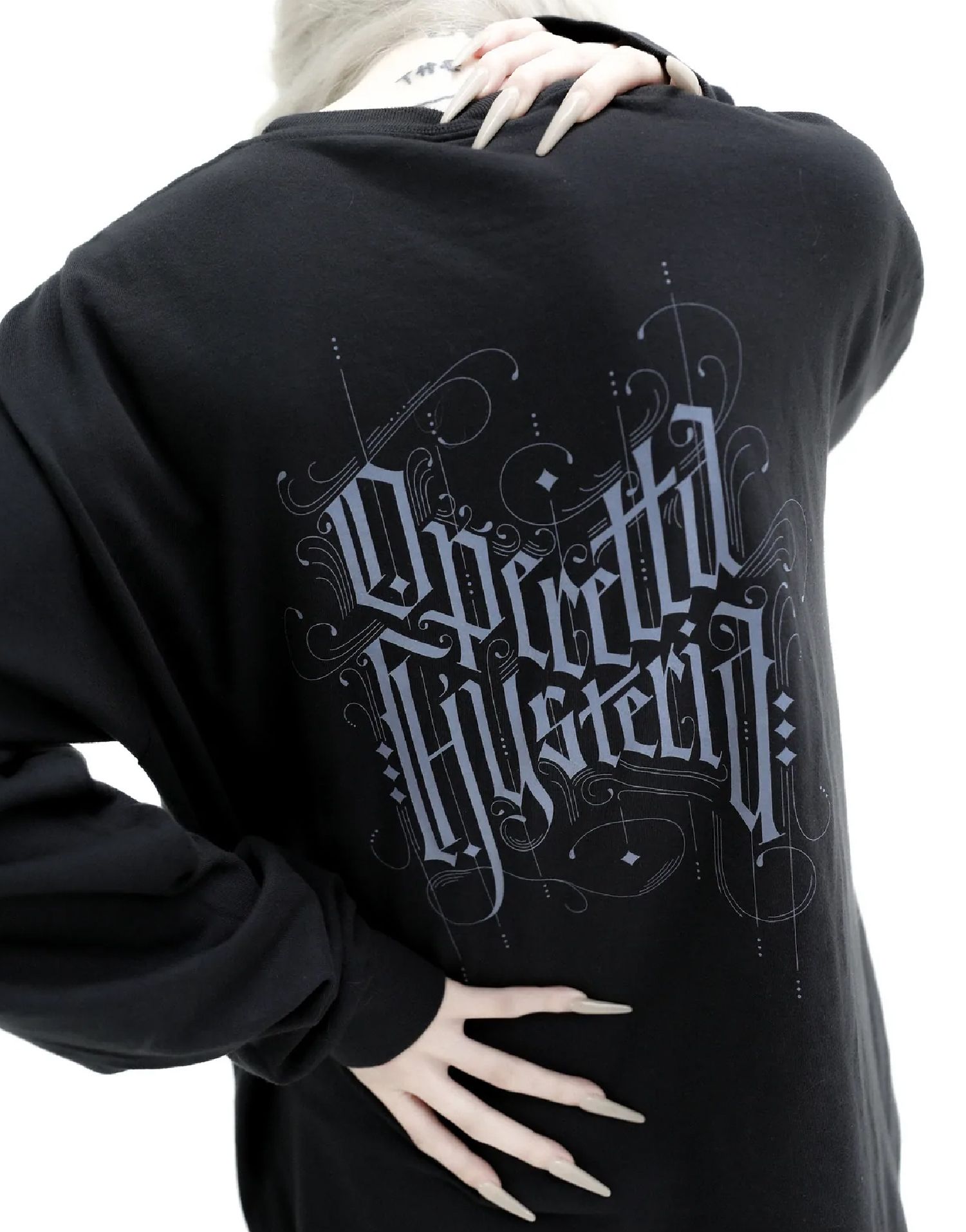 Nina Utashiro wearing a black shirt with gothic silver lettering on the back, hand on hip