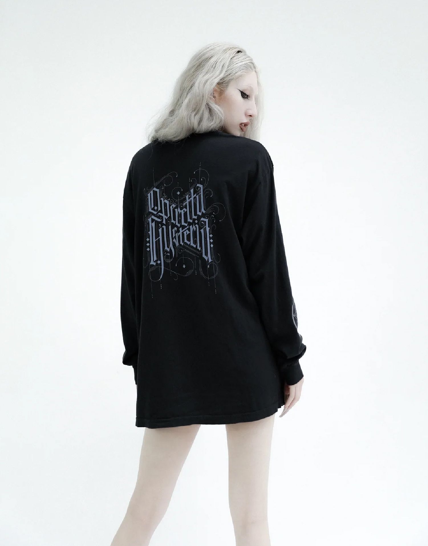 Nina Utashiro in a black oversized shirt, seen from behind, with blonde hair against a white background.