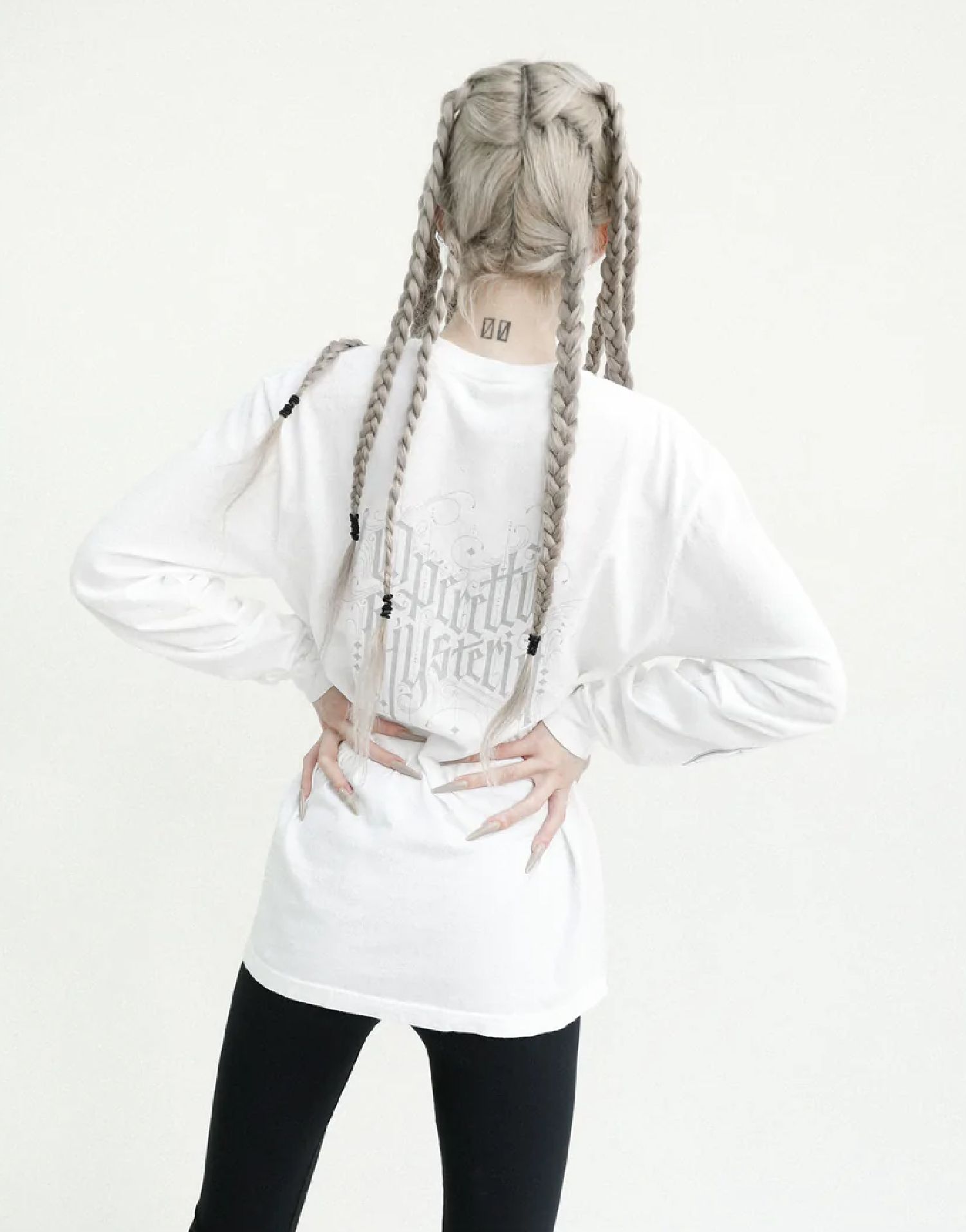 Nina Utashiro with long braided hair posing in white oversized shirt and black leggings, hands on hips