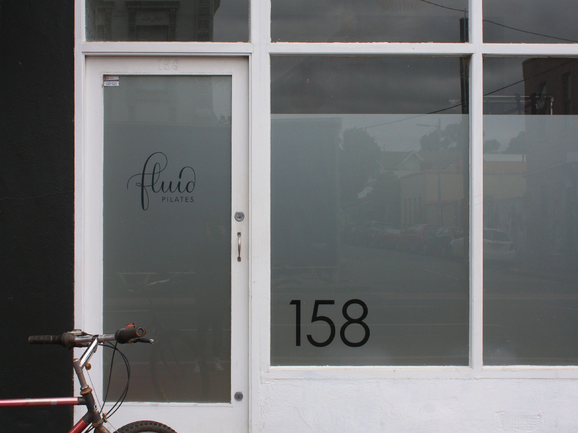 Storefront with frosted glass door and windows, bicycle parked in front, number 158 visible.