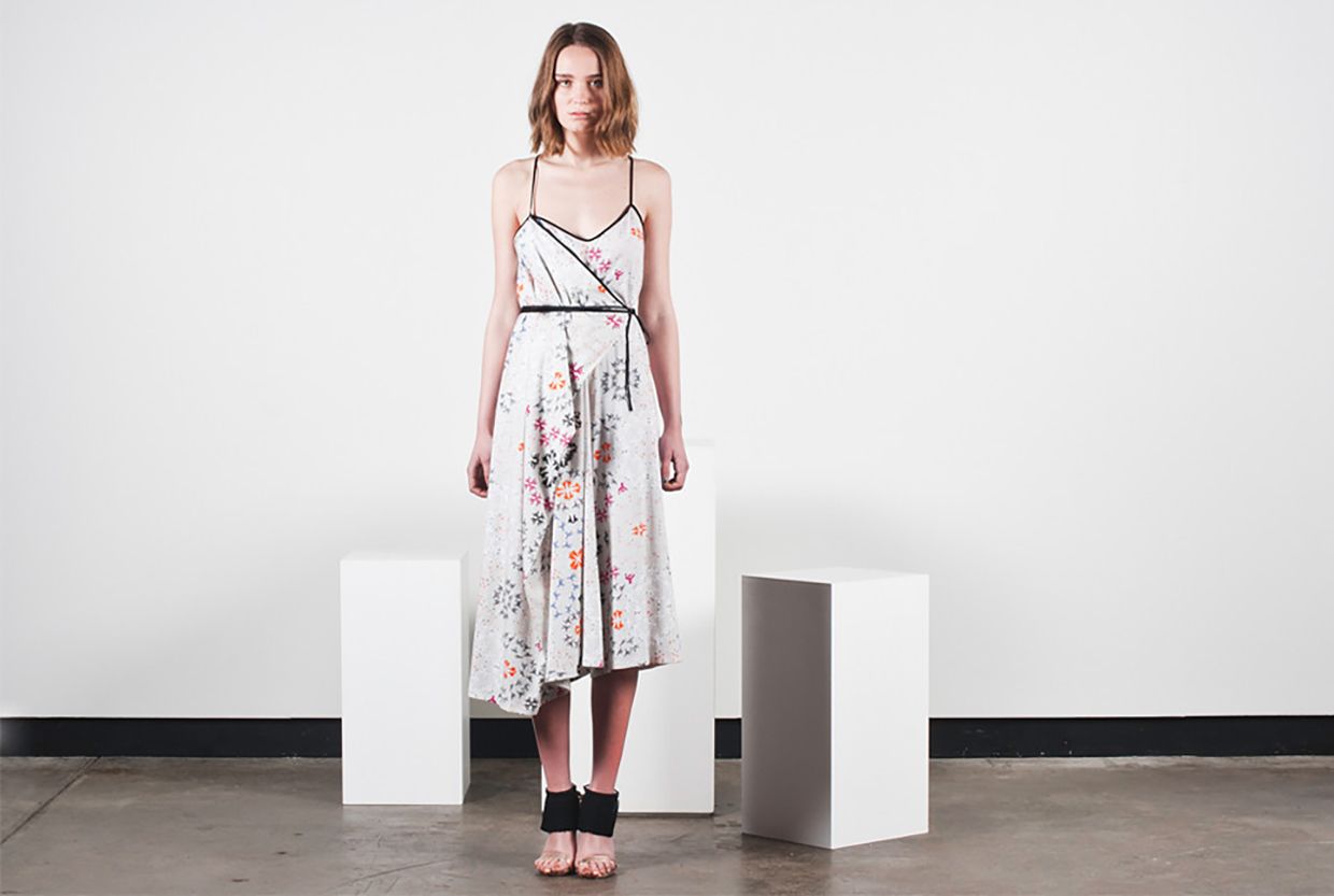 Woman in a white floral dress standing between two white pedestals in a minimalist studio.