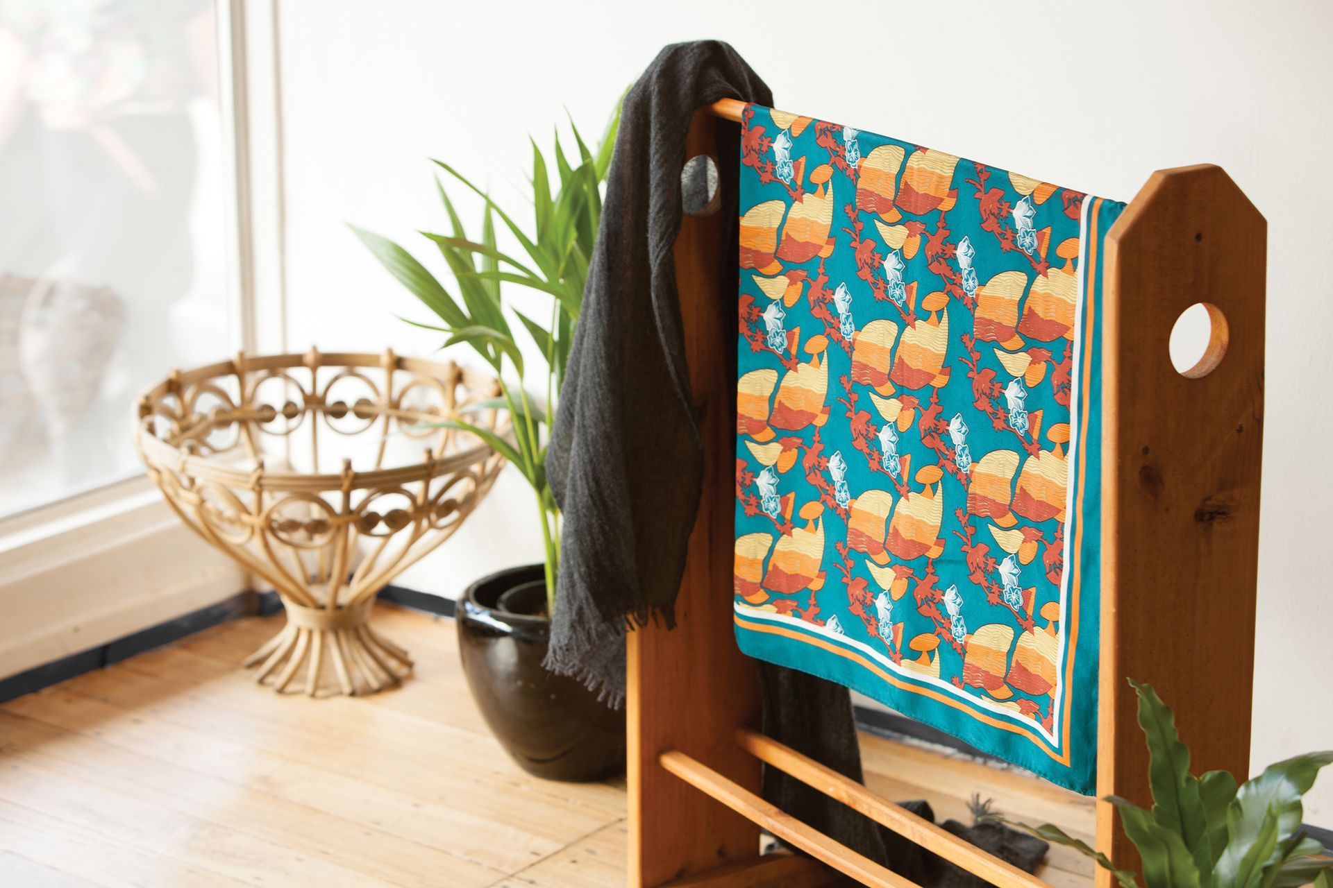 Colorful patterned fabric draped over a wooden stand beside a plant on a sunlit windowsill