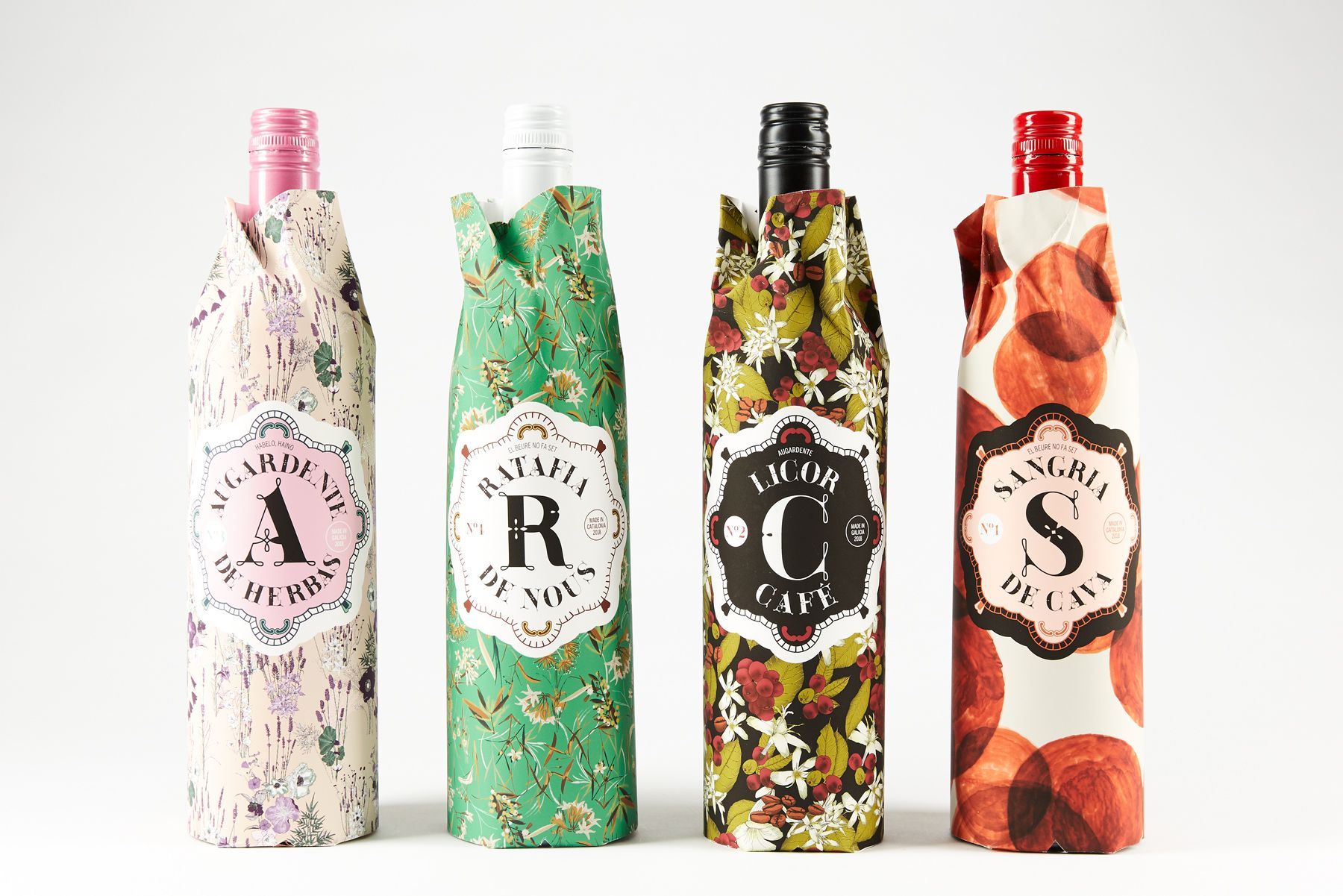 Four decorated wine bottles with patterned wraps labeled A, R, C, and S on a white background