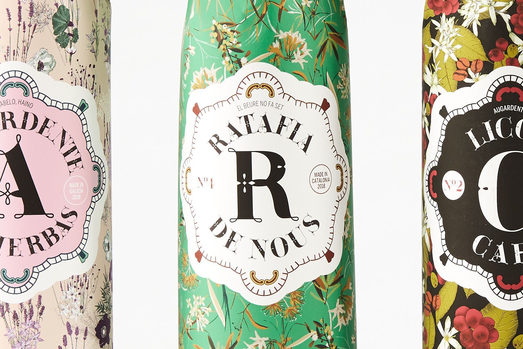 Three decorative bottles with floral patterns and large monogram labels in pink, green, and black.