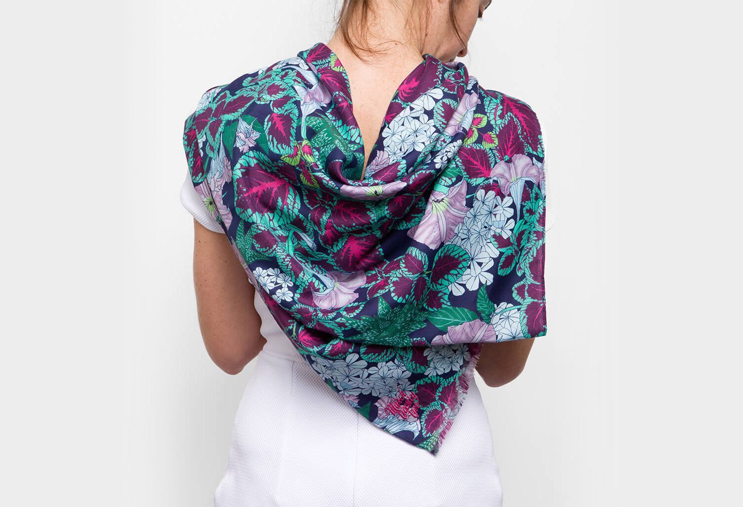 Woman wearing a colorful floral scarf draped over a white top, shown from the back.