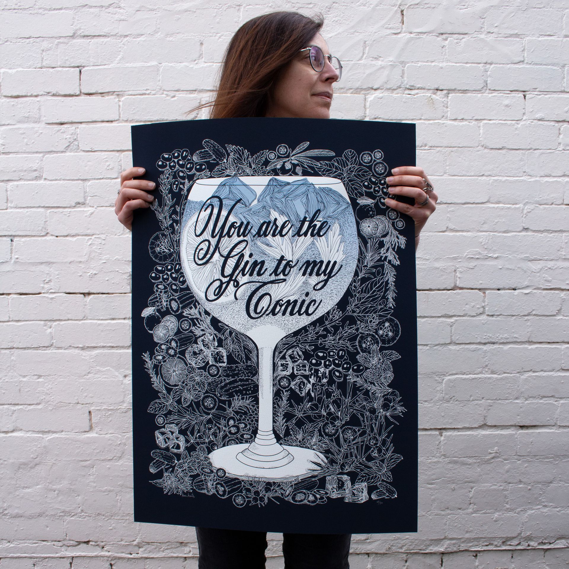 Woman holding a black poster with a white gin glass and the text “You are the Gin to my Tonic”
