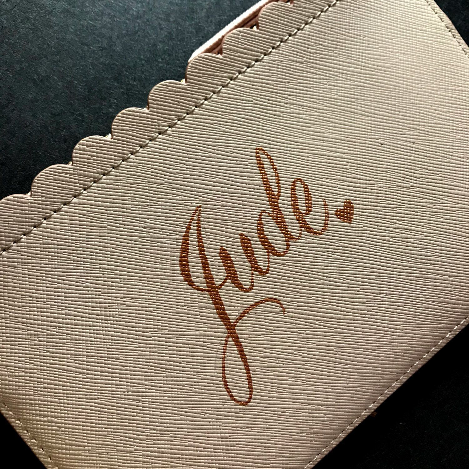 Close-up of a beige scalloped pouch with the name “Jade” embroidered in brown script.