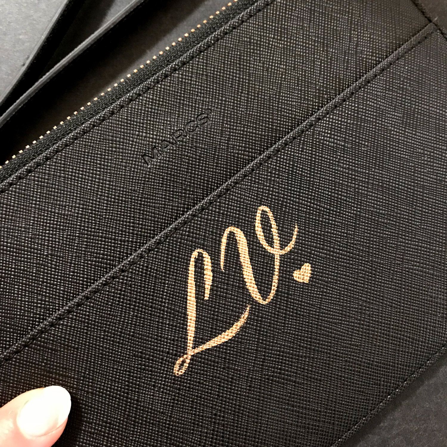 A black textured leather accessory featuring the gold embossed cursive letters