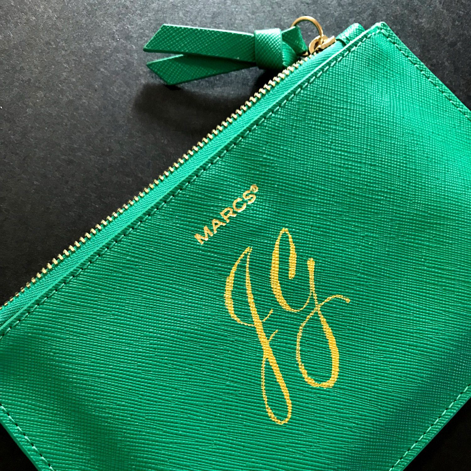 Green leather zipper pouch with gold initials and a tassel on a dark surface