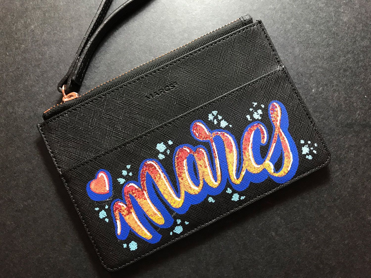 Black wristlet purse with colorful glitter script reading “aries” on a dark background
