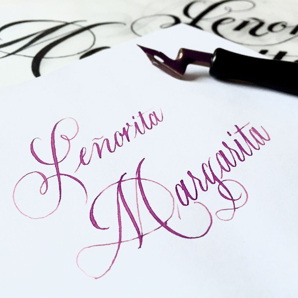 Pink calligraphy signature on white paper with a fountain pen at the top right