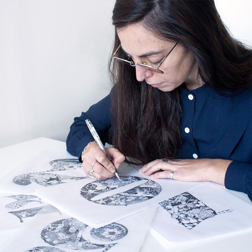 Maria Montes sketching black-and-white design studies on paper at a desk