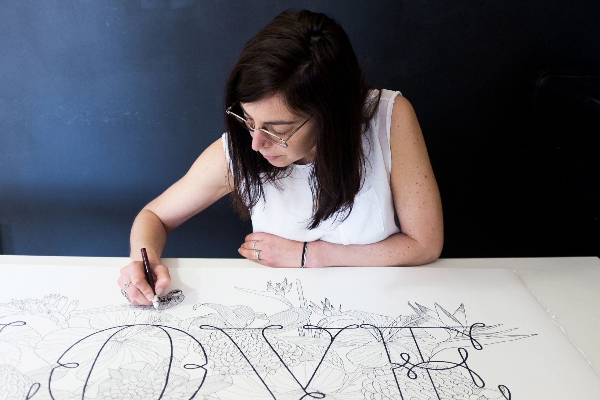 Maria Montes drawing on a large white sheet at a table with black ink.
