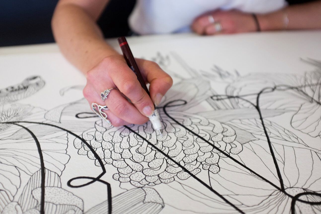 Hand drawing a detailed floral pattern with a pencil on white paper