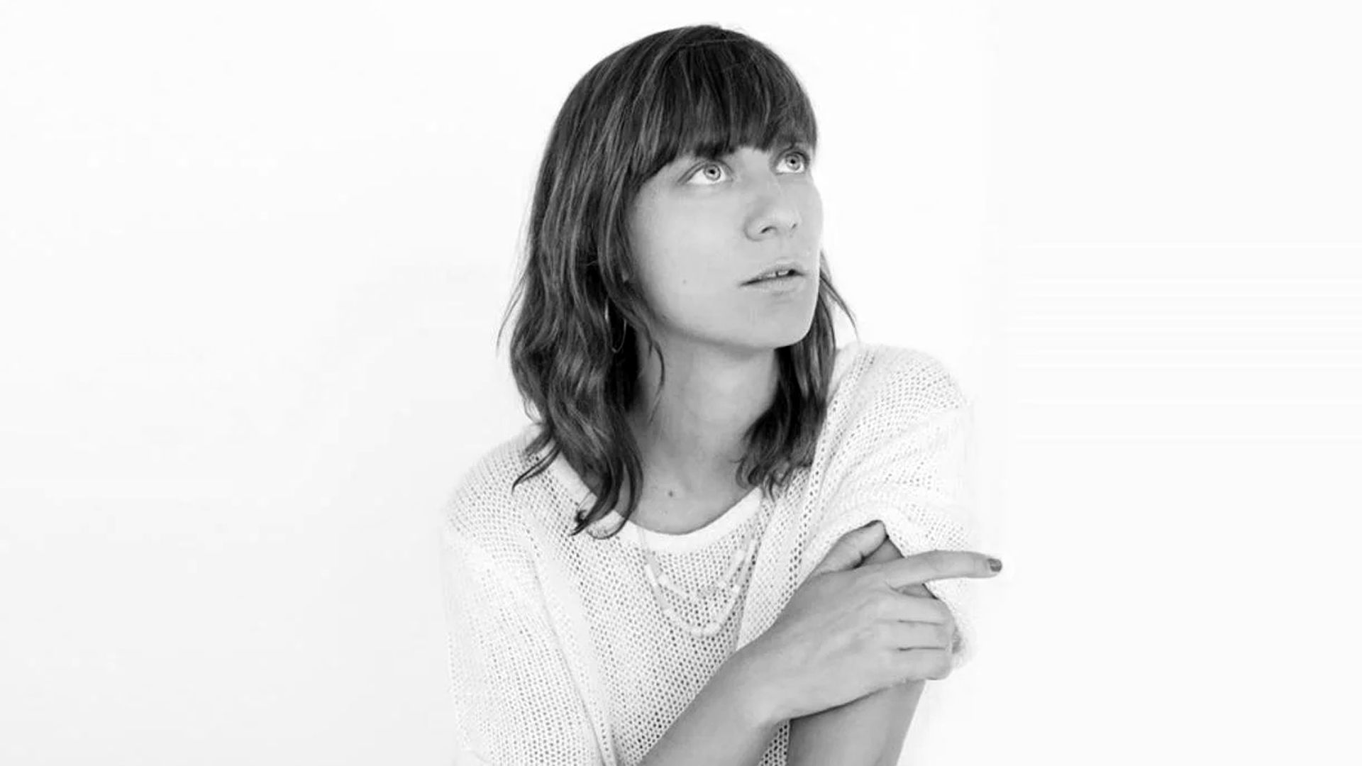 Woman in a white sweater looking upward, arms crossed, against a plain white background
