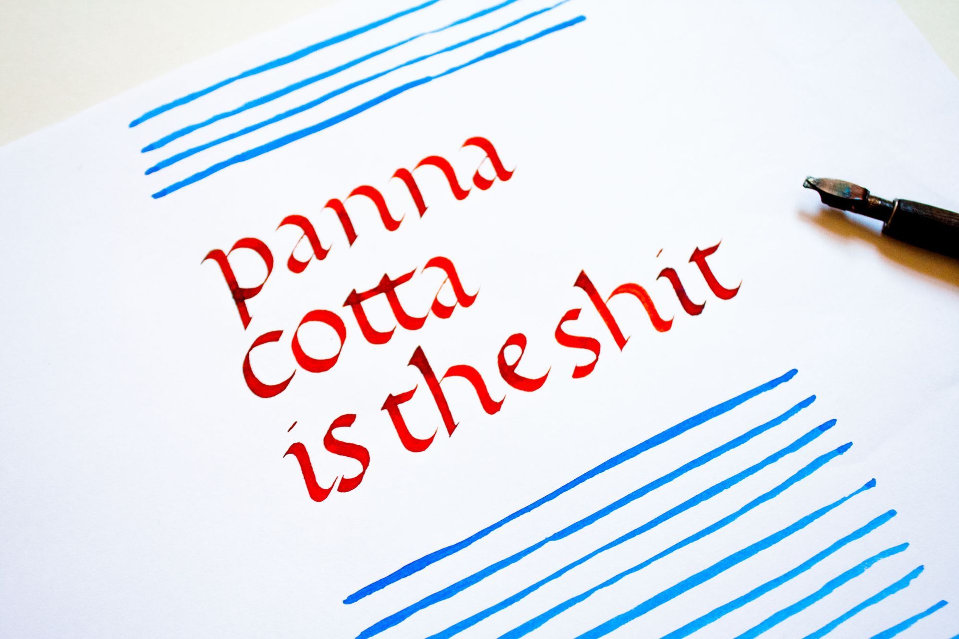 Red text reading “panna cotta is the shit” on a white page with blue lines and a pen nearby
