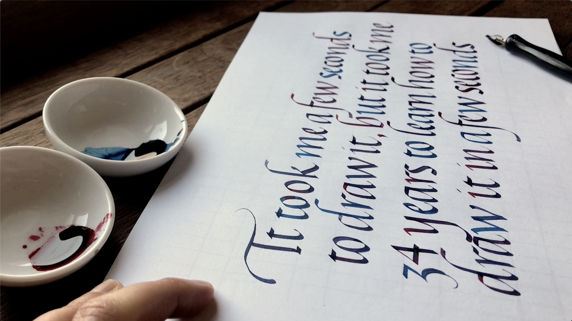 A hand-lettered calligraphy sheet beside two small bowls of ink on a table.