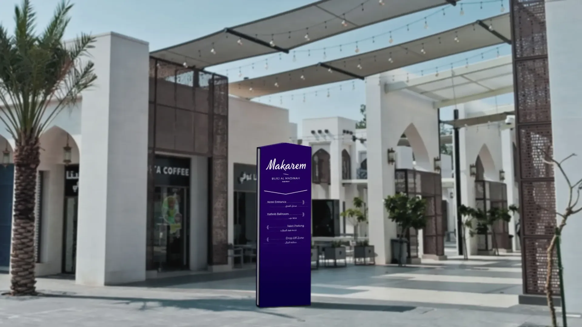 Outdoor shopping plaza entrance with a purple directory sign, white storefronts, and a shaded canopy overhead