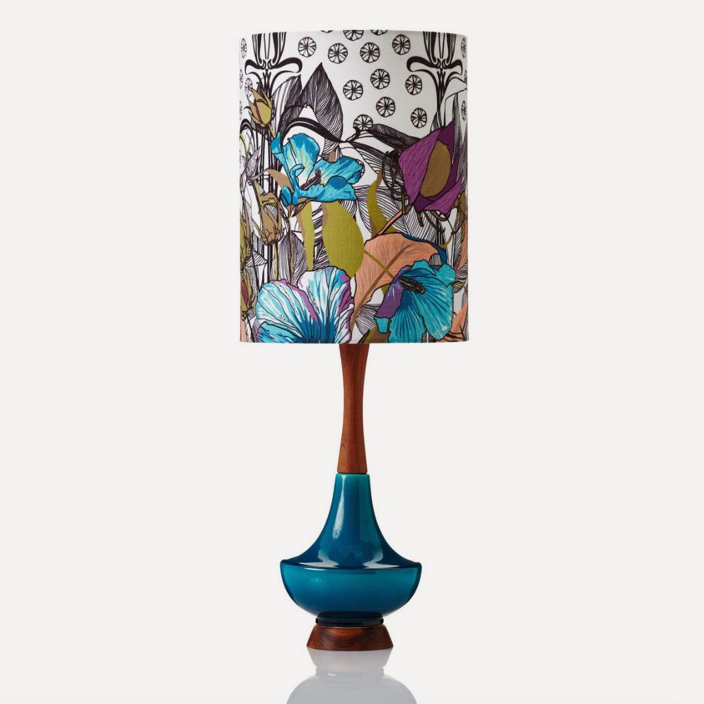 A table lamp with a dark wood base, a blue ceramic teardrop body, and a cylindrical shade with a colorful floral pattern.