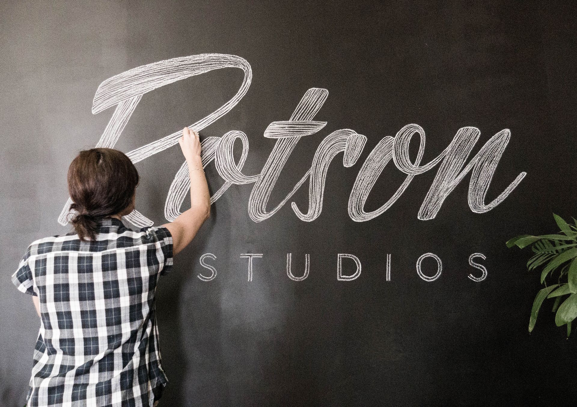 Person painting the “Petron Studios” sign on a black wall.