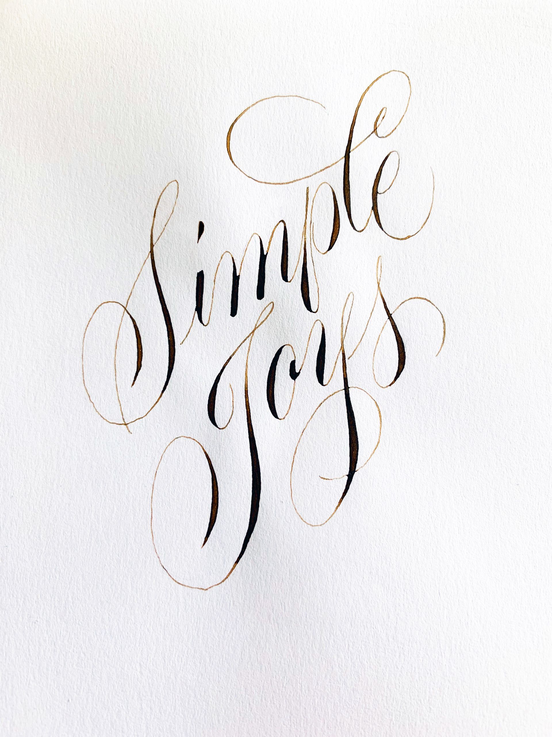 Hand-lettered gold script reading “Simple Joys” on white paper