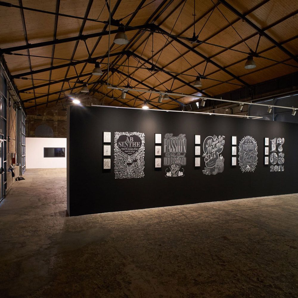 Interior of an art gallery with a black exhibition wall displaying framed black-and-white prints under warm ceiling lights