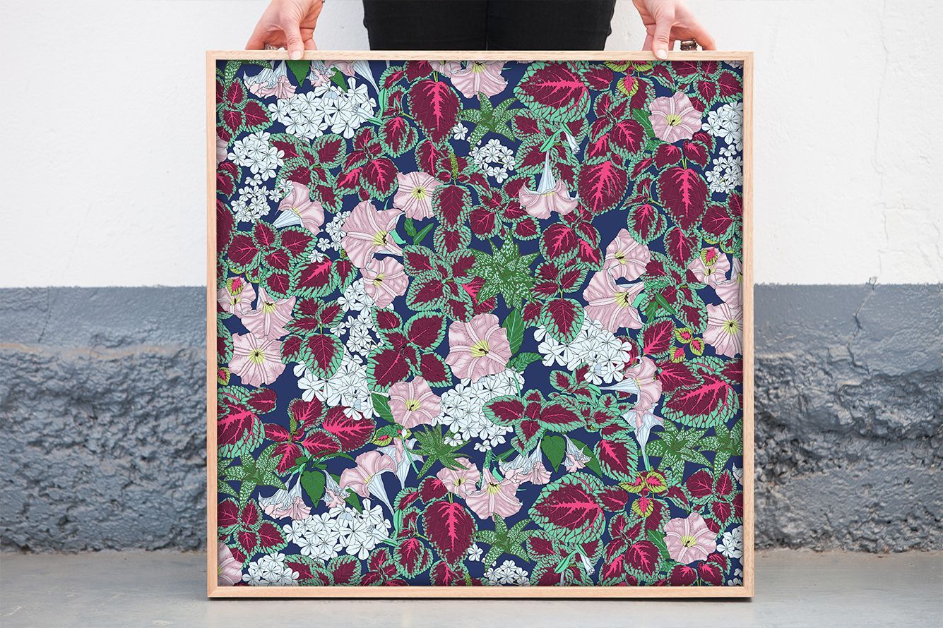 Square floral-patterned tote bag with pink handles held against a white wall and gray floor