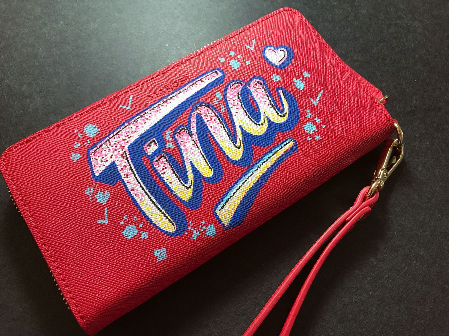 Red Twiggy logo zip pouch with red wrist strap on a gray surface