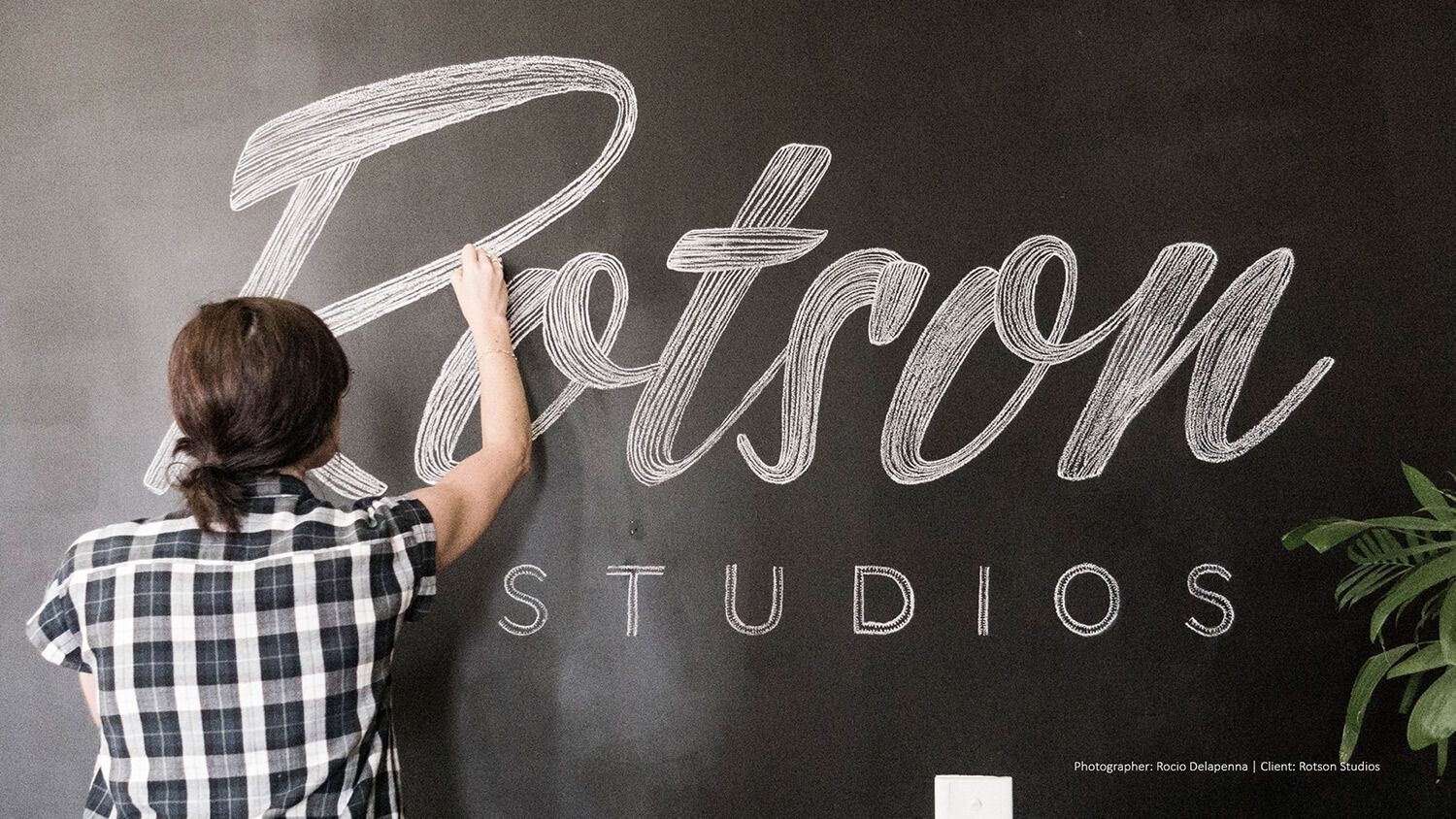 Person painting the word “Rotson” on a black wall with “STUDIOS” underneath