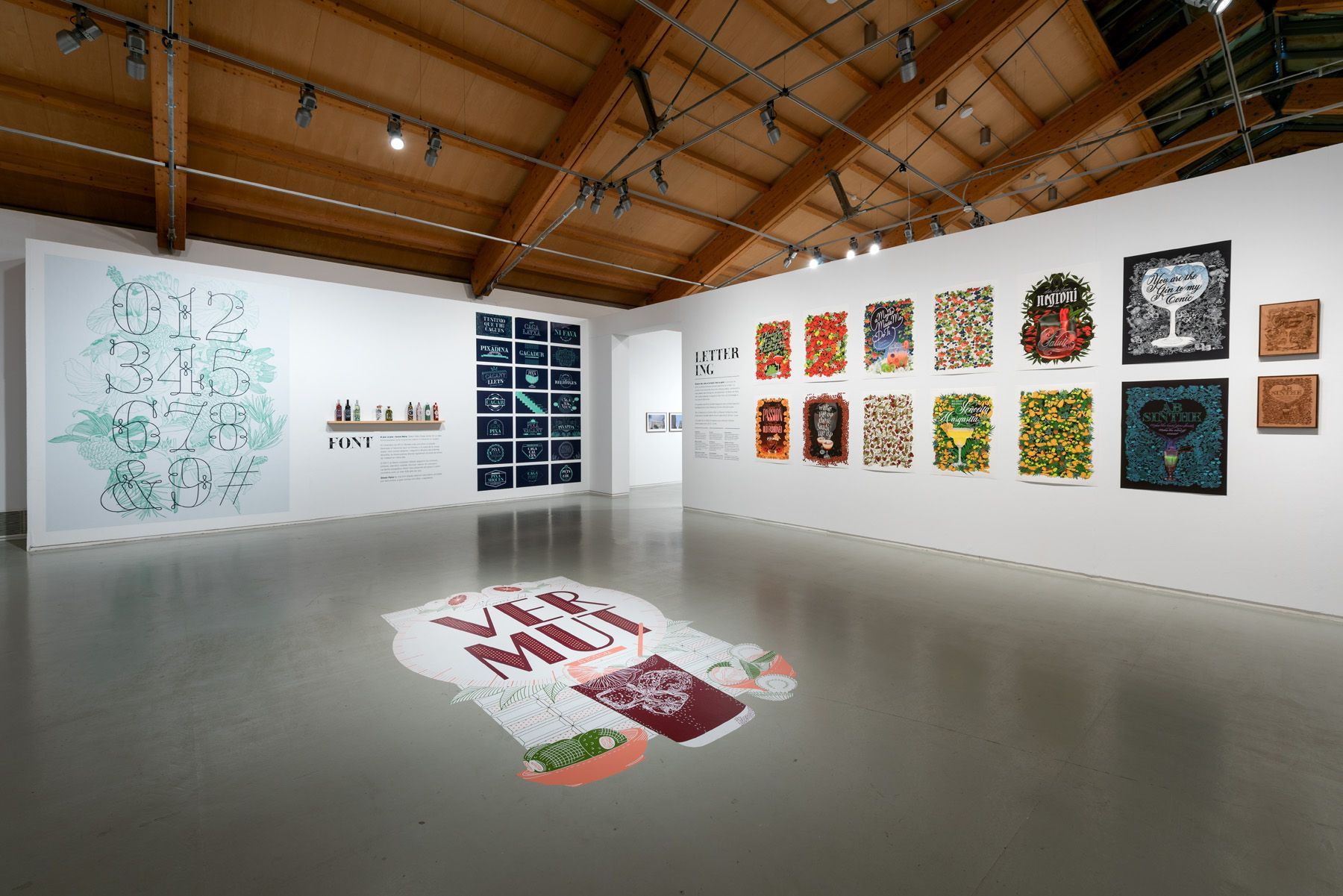 Art gallery with colorful abstract wall pieces and floor installations in a bright room with a wood-beamed ceiling