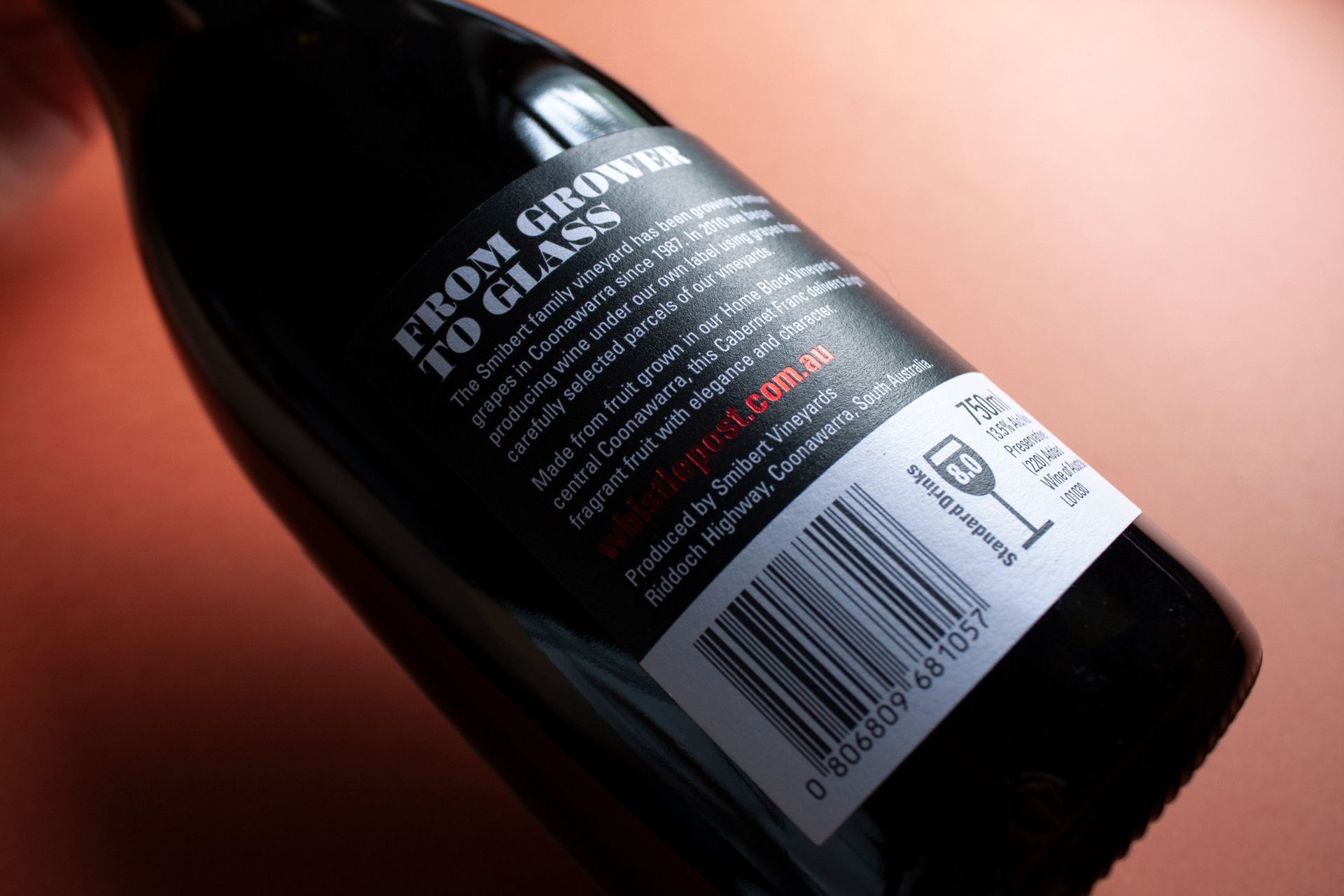 Close-up of a dark wine bottle with a white label and barcode, lying on a warm orange surface