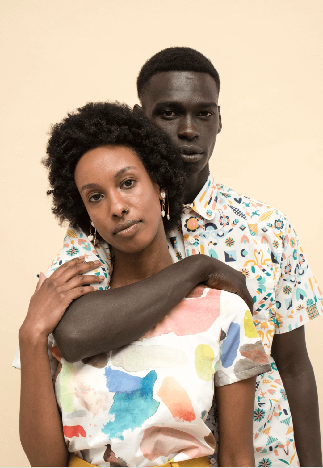A person wearing a short-sleeved white button-down shirt featuring a colorful, patterned geometric print against a beige backdrop.