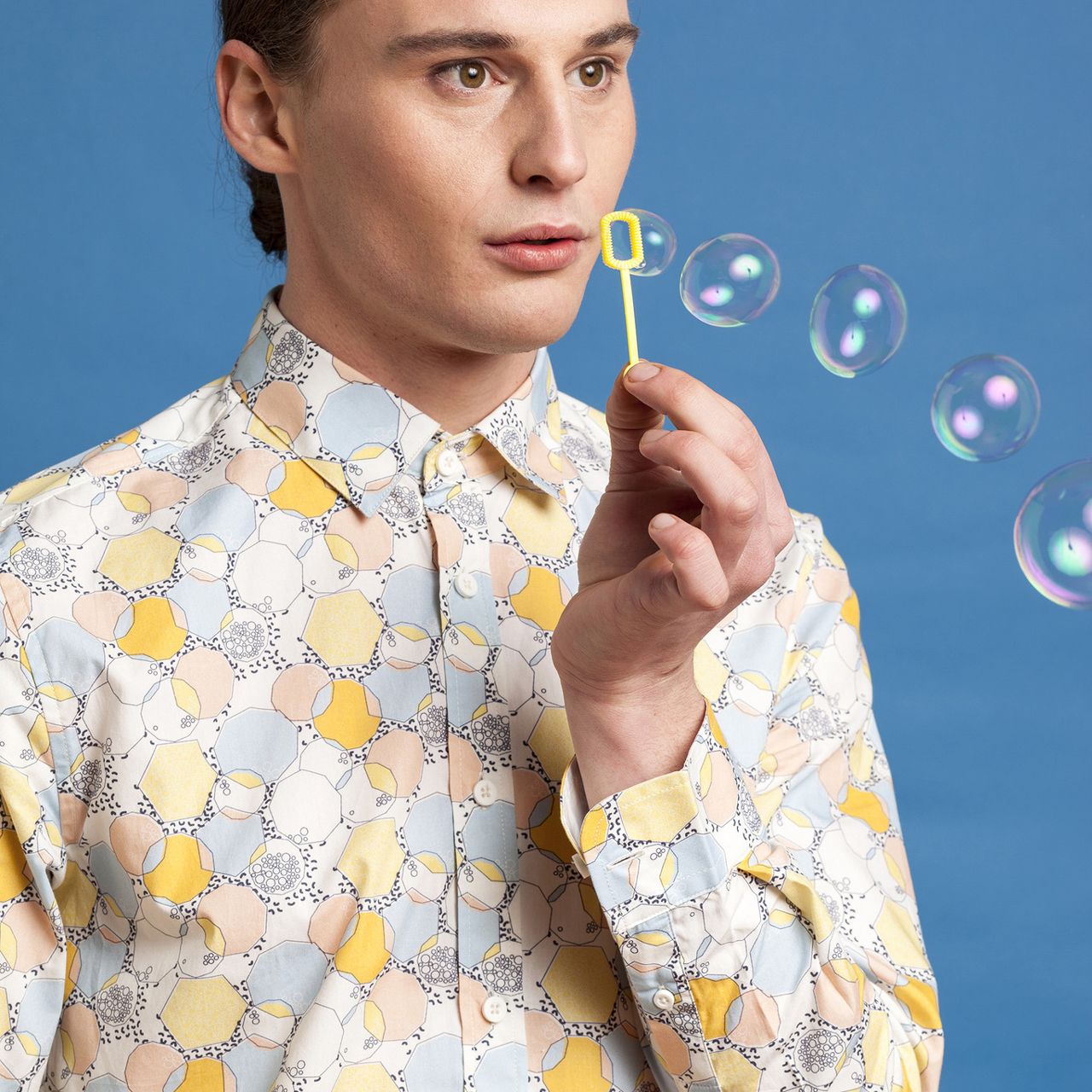 Person in patterned shirt blowing bubbles against a blue background
