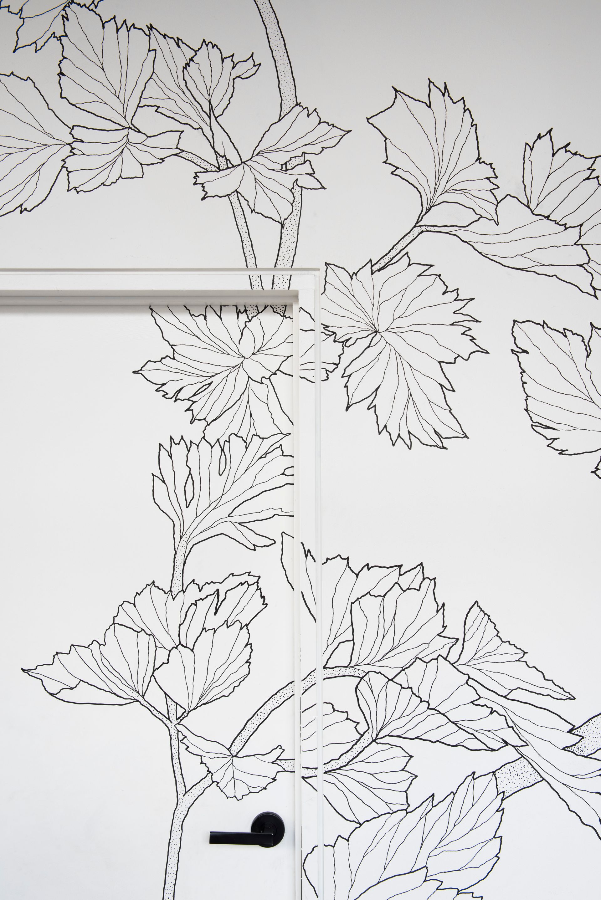 Black-and-white floral line art wallpaper on a white door with a black handle