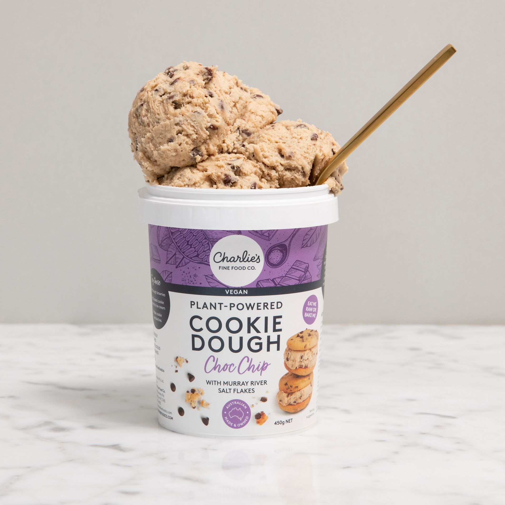 Tub of chocolate chip cookie dough with a wooden spoon, on a light background