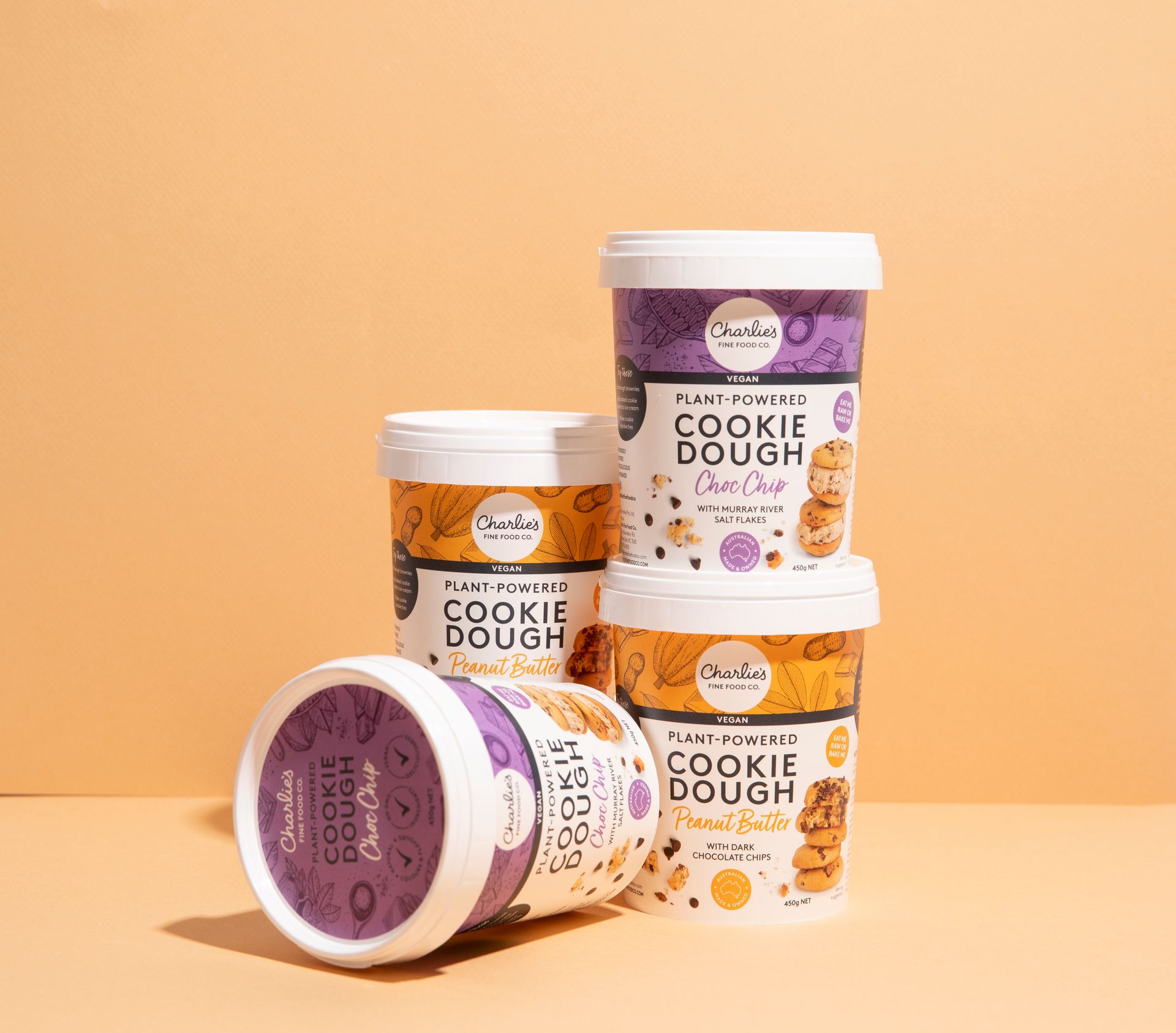 Assorted cookie dough tubs stacked on a peach background, with one lid facing forward.