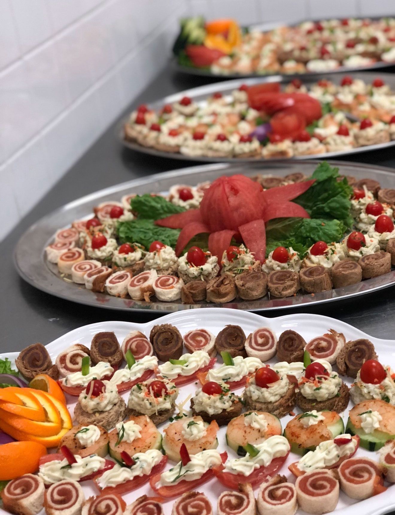 Buffet of appetizers: mini sandwiches, rolls, topped with cream cheese, tomatoes, and garnishes on platters.