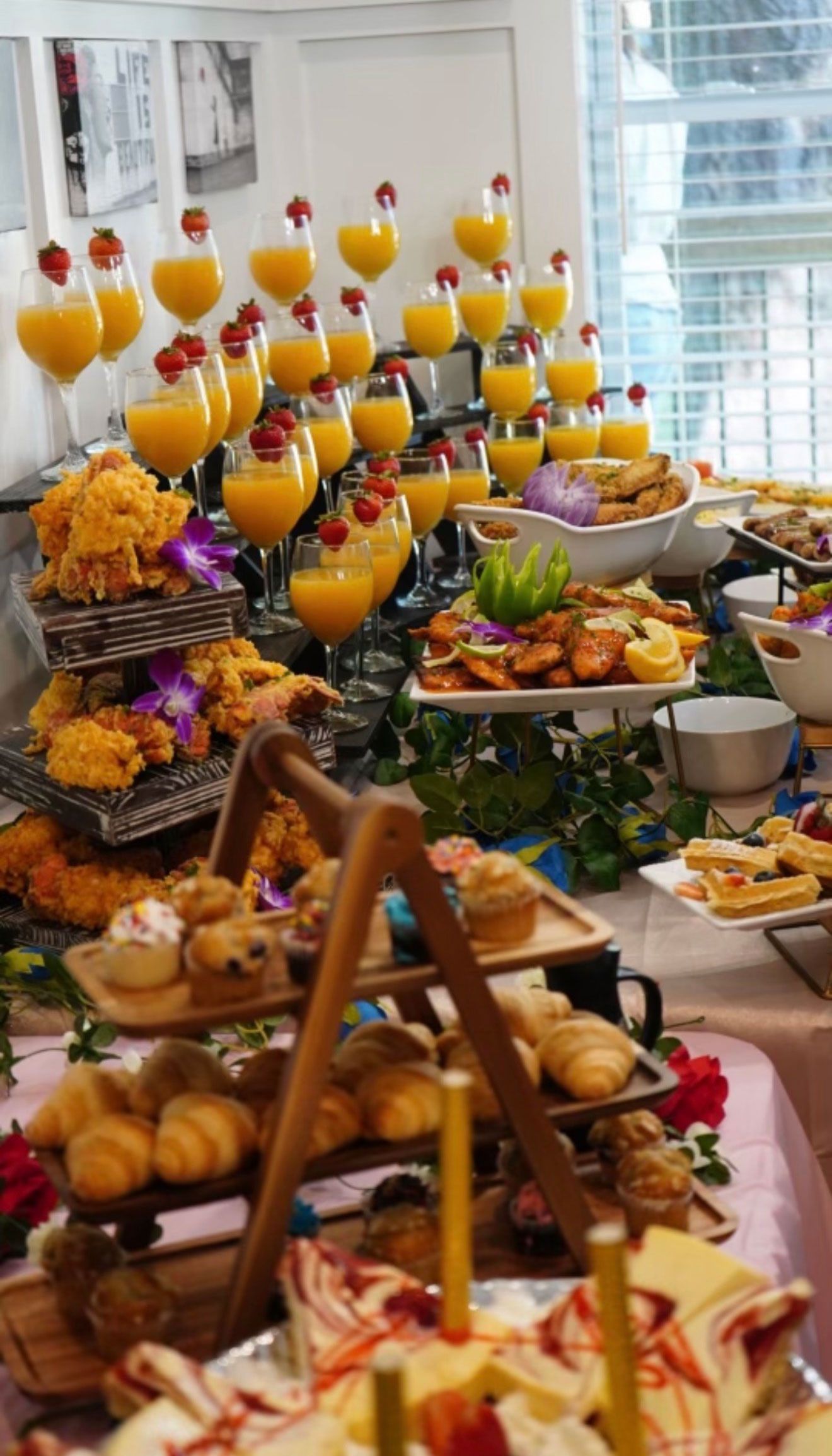 Buffet table with an array of food and drinks. Includes pastries, juice with berries, and decorative floral arrangements.