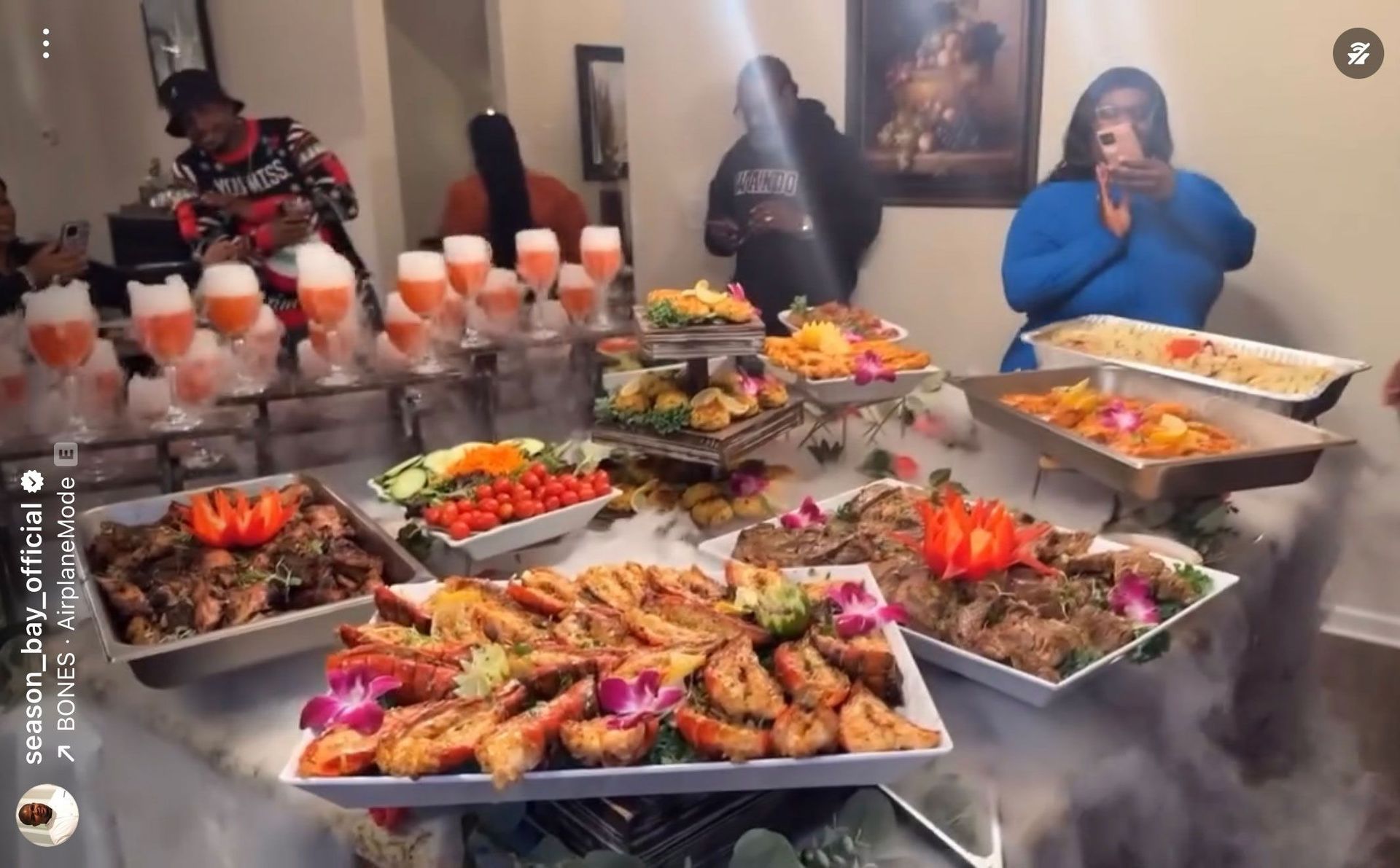 A lavish buffet table with food and drinks, people gathering, colorful dishes, and dry ice effect.