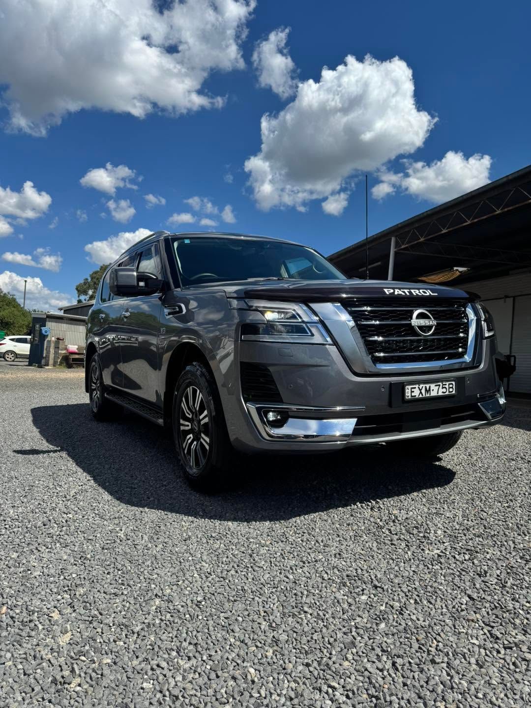 Black Nissan SUV Parked on Gravel Under a Bright Blue Sky with Clouds — Diamond Glow Auto Detailing in Armidale, NSW