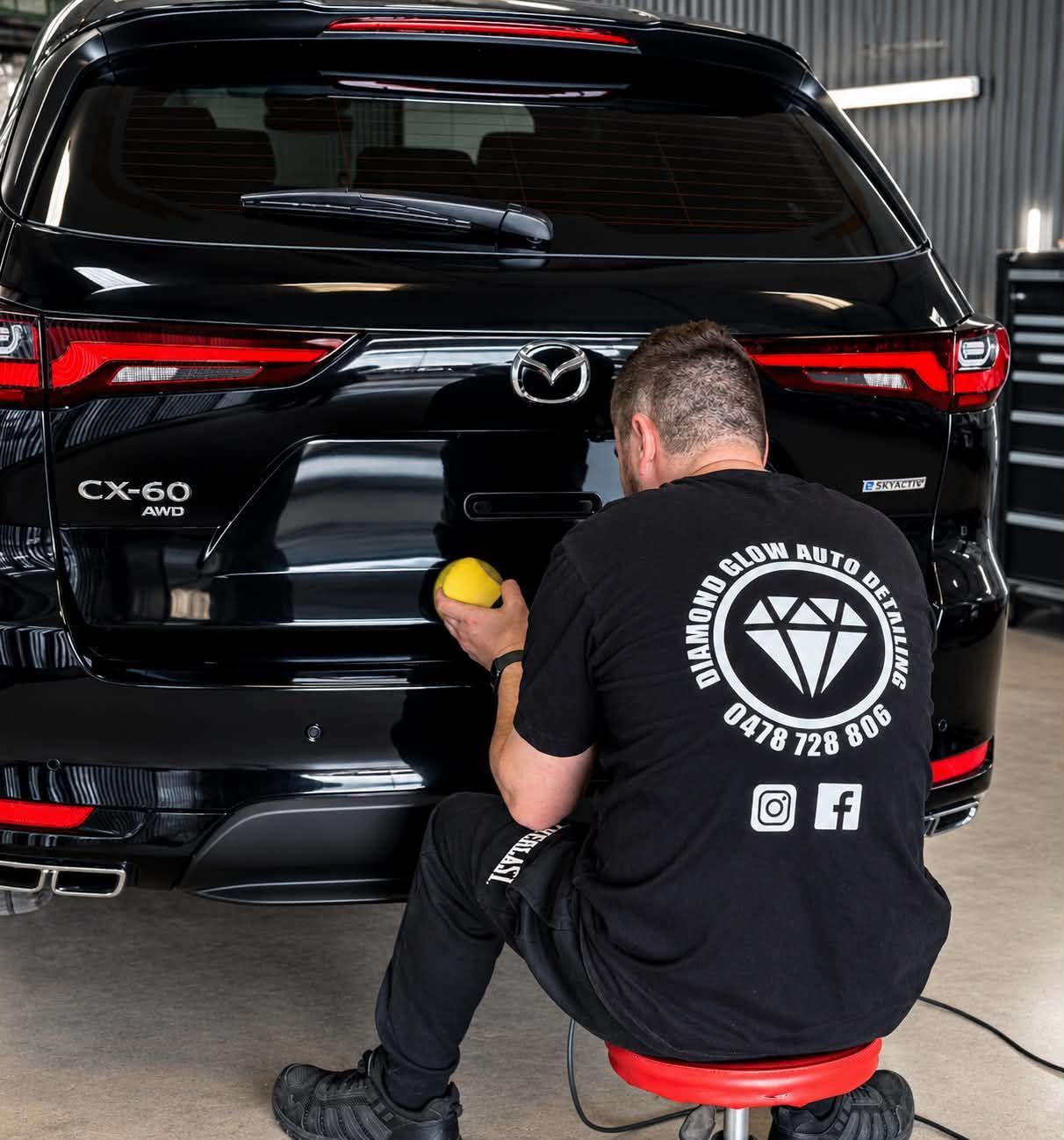 Detailer polishing the rear of a black Mazda CX-60 in a garage— Diamond Glow Auto Detailing in Armidale, NSW